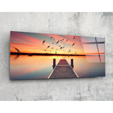 Uccelli in volo sul molo al tramonto quadro in vetro